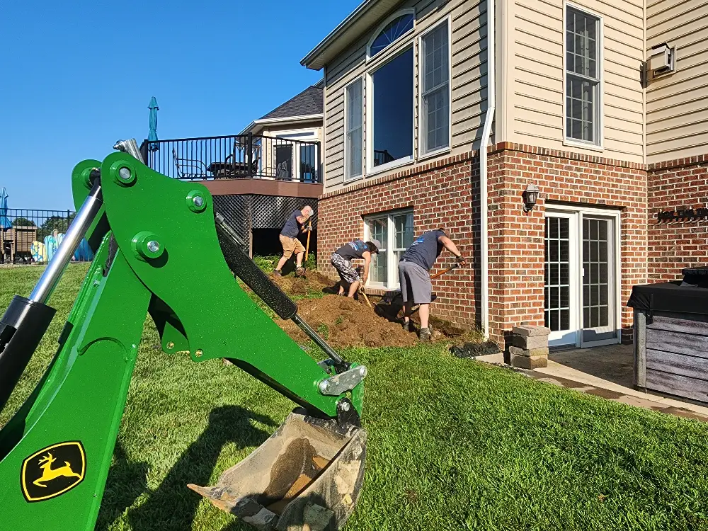 Excavation crew installing exterior drainage and grading improvements around a home's foundation to prevent basement flooding